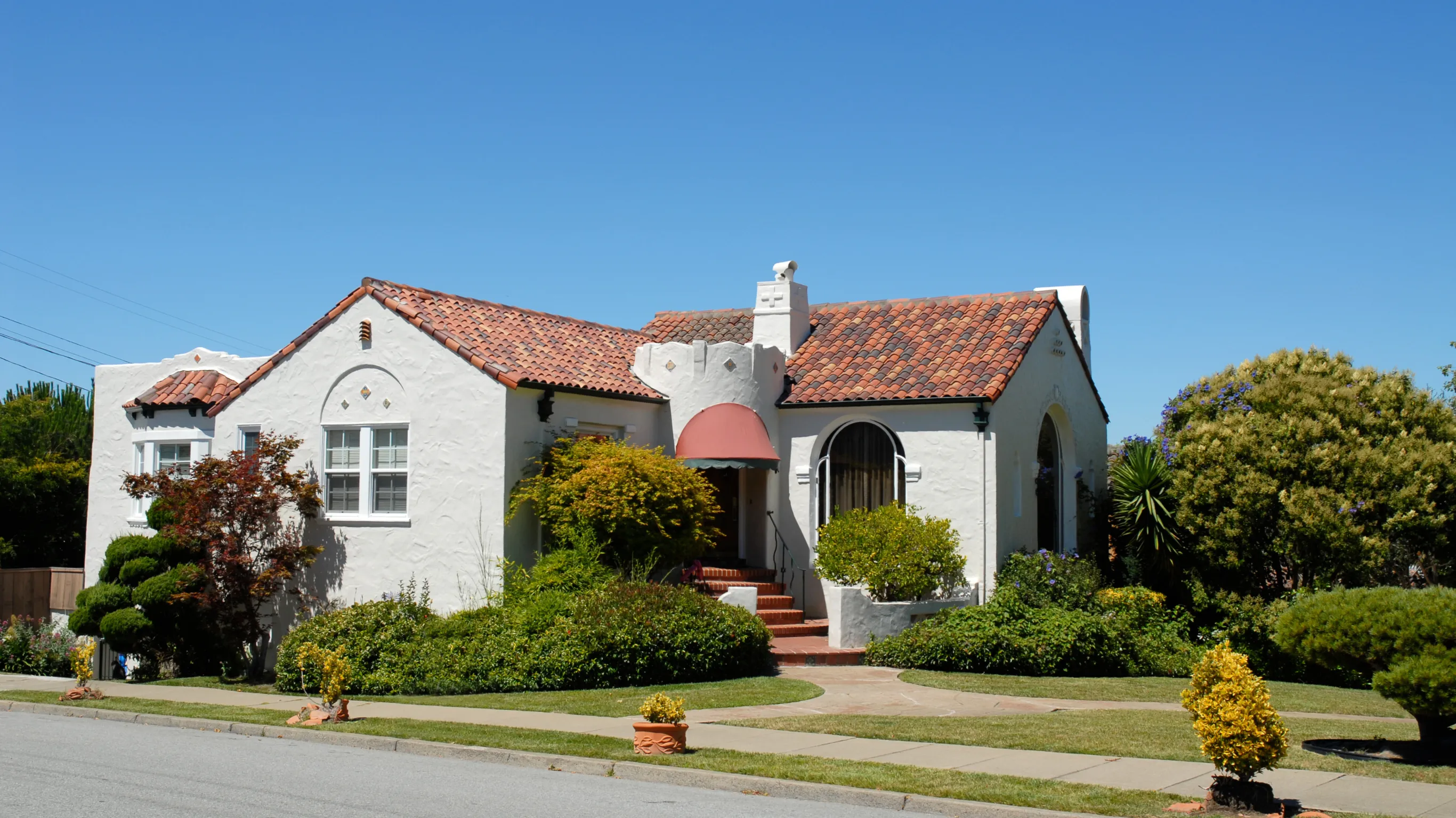 Before photo of room addition project in Los Angeles with original Spanish-style home exterior, stucco walls, red tile roof, front landscaping, and existing residential structure before expansion