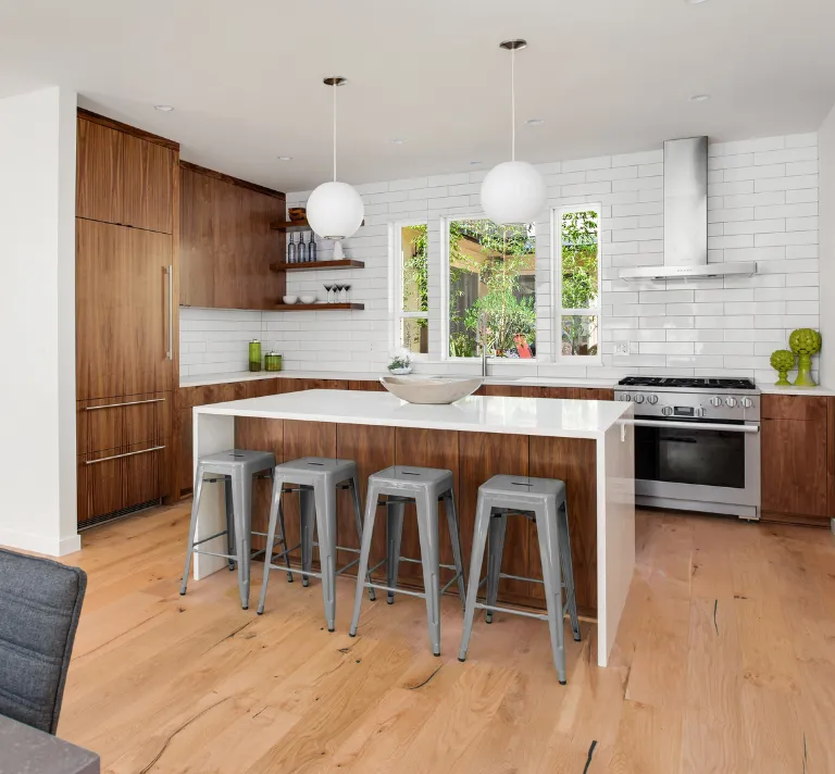 Kitchen remodeling in Los Angeles with modern wood cabinets, white island countertop, subway tile backsplash, pendant lighting, and open kitchen layout